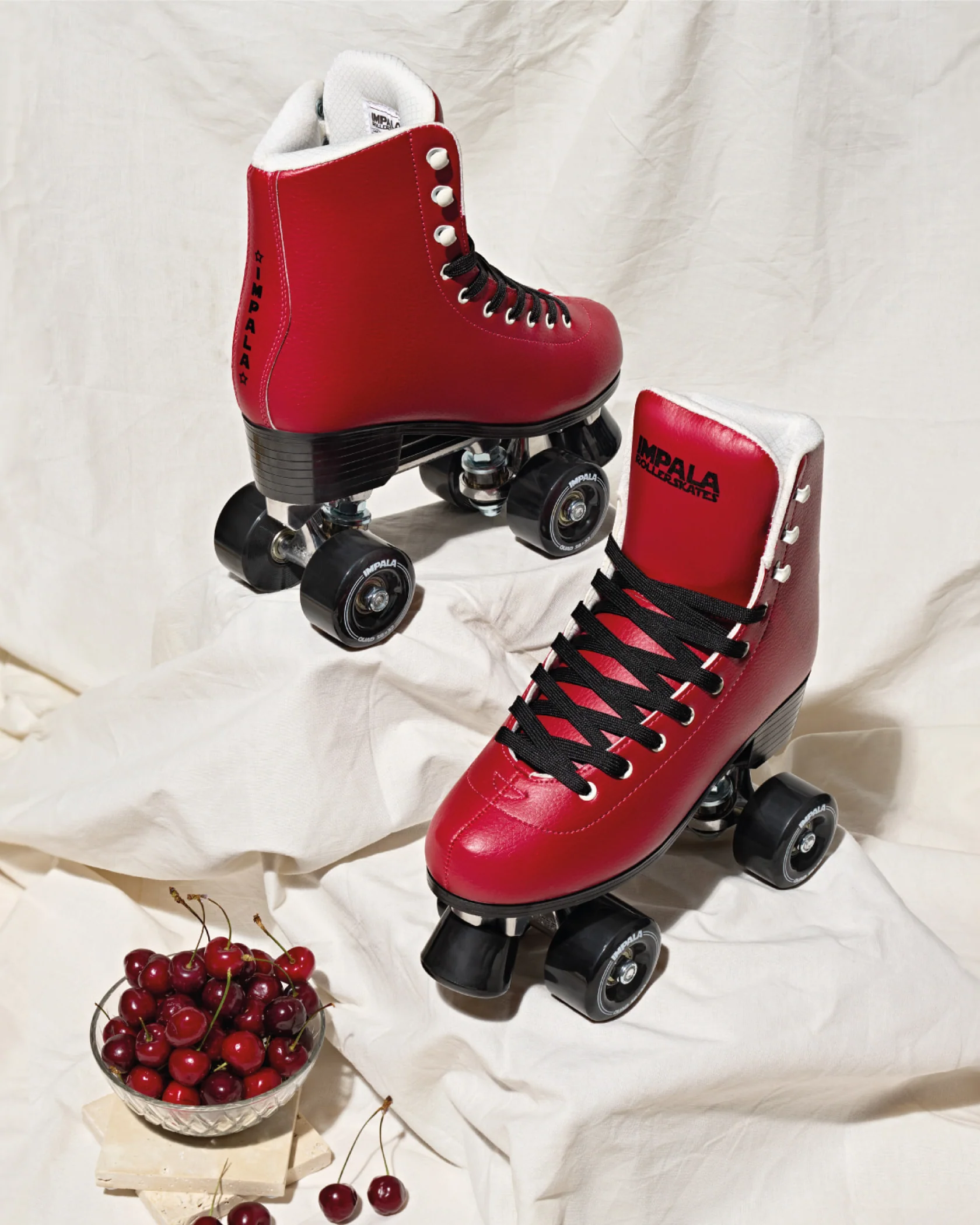 A pair of cherry red Impala roller skates beside a bowl of cherries